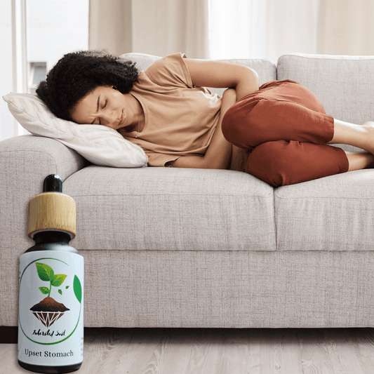picture of a woman on the couch with a stomach ache and a bottle of inherited soils upset stomach natural relief oil